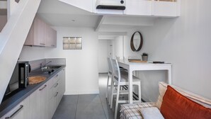 Eine kompakte Küche mit Mikrowelle, Spüle und Schränken, ein Essbereich mit Tisch und Stühlen sowie ein Bett mit kariertem Überwurf.