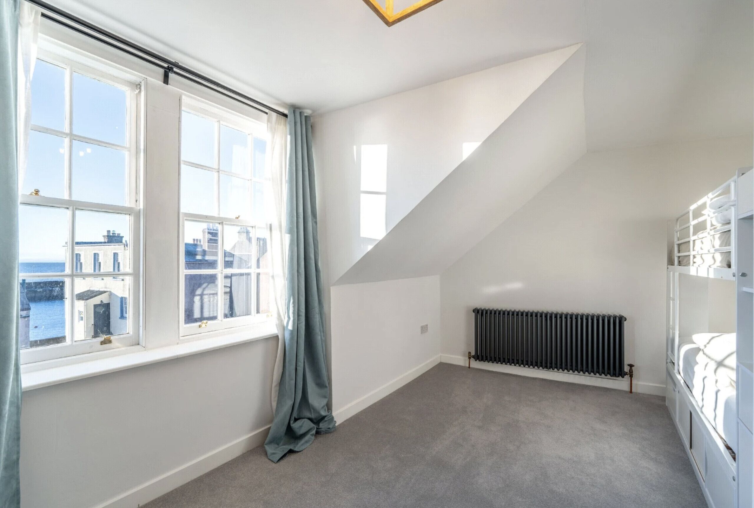 A room with a sloped ceiling, large windows, a radiator, and a bunk bed.