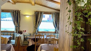 Un coin repas rustique avec des tables et des chaises en bois, un banc et une vue sur l’extérieur.