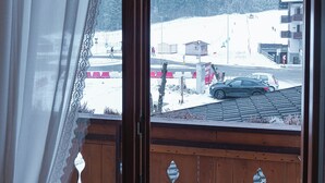Une pièce dotée d’un balcon en bois, offrant une vue sur un paysage enneigé, et d’une fenêtre avec un rideau.