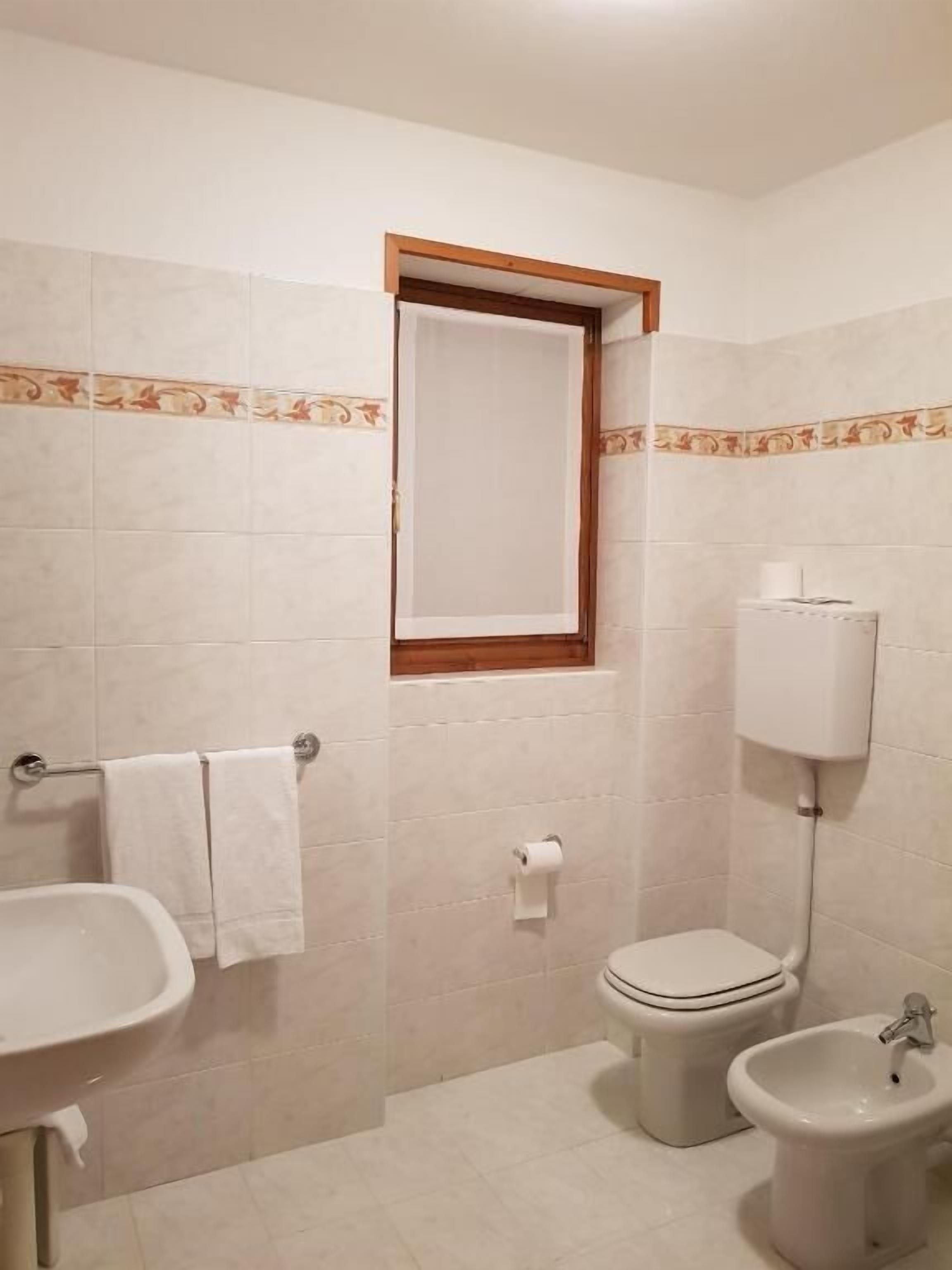 A bathroom with a sink, toilet, bidet, and a window with a wooden frame.