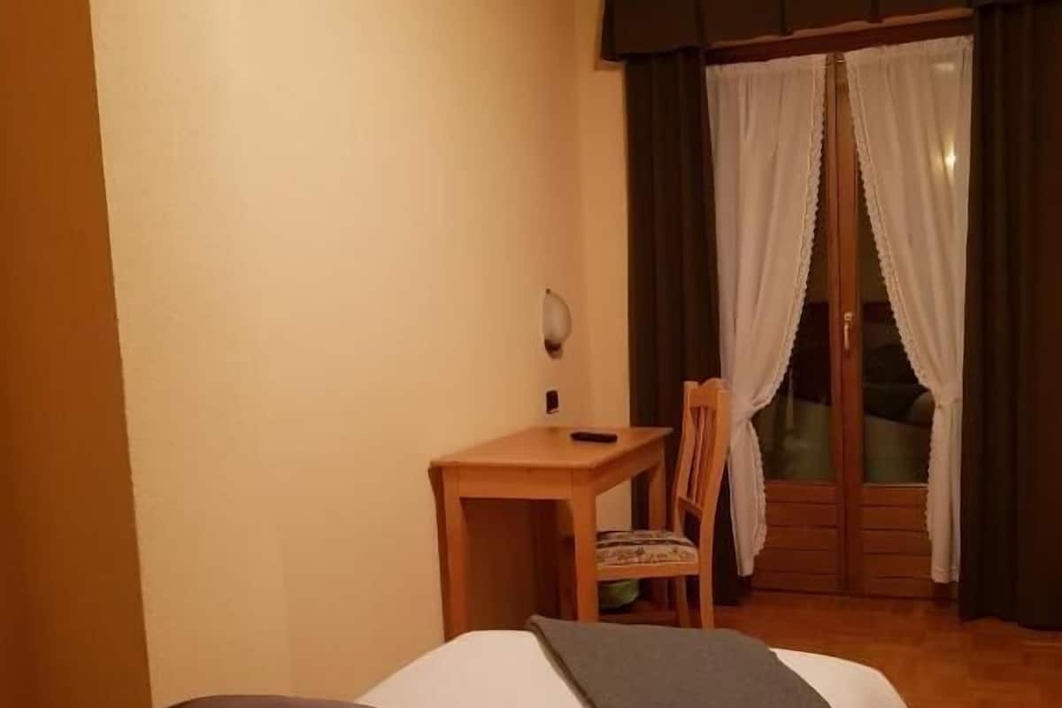 Habitación de hotel con cama, escritorio, silla y vistas al exterior a través de cortinas.