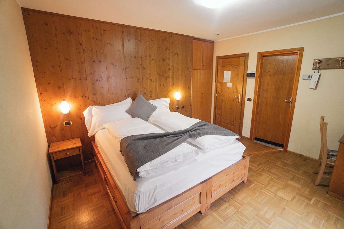 Una cama con estructura de madera, ropa de cama blanca, dos lámparas de noche y una mesita de noche de madera.