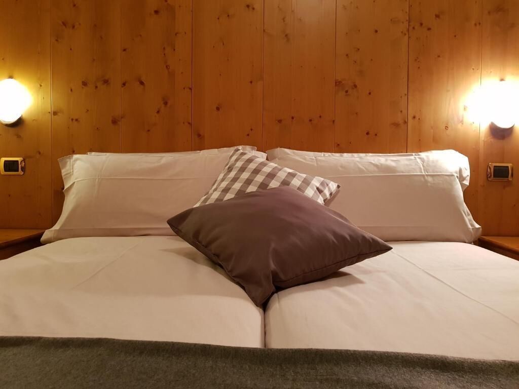 Ein Doppelbett mit weißen Leinen und einem braunen Kopfkissen, vor einer Holzwand mit zwei Wandleuchten.