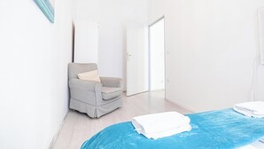 Una camera d'albergo con una poltrona a quadretti, una coperta blu e una porta bianca che dà su un'altra stanza.