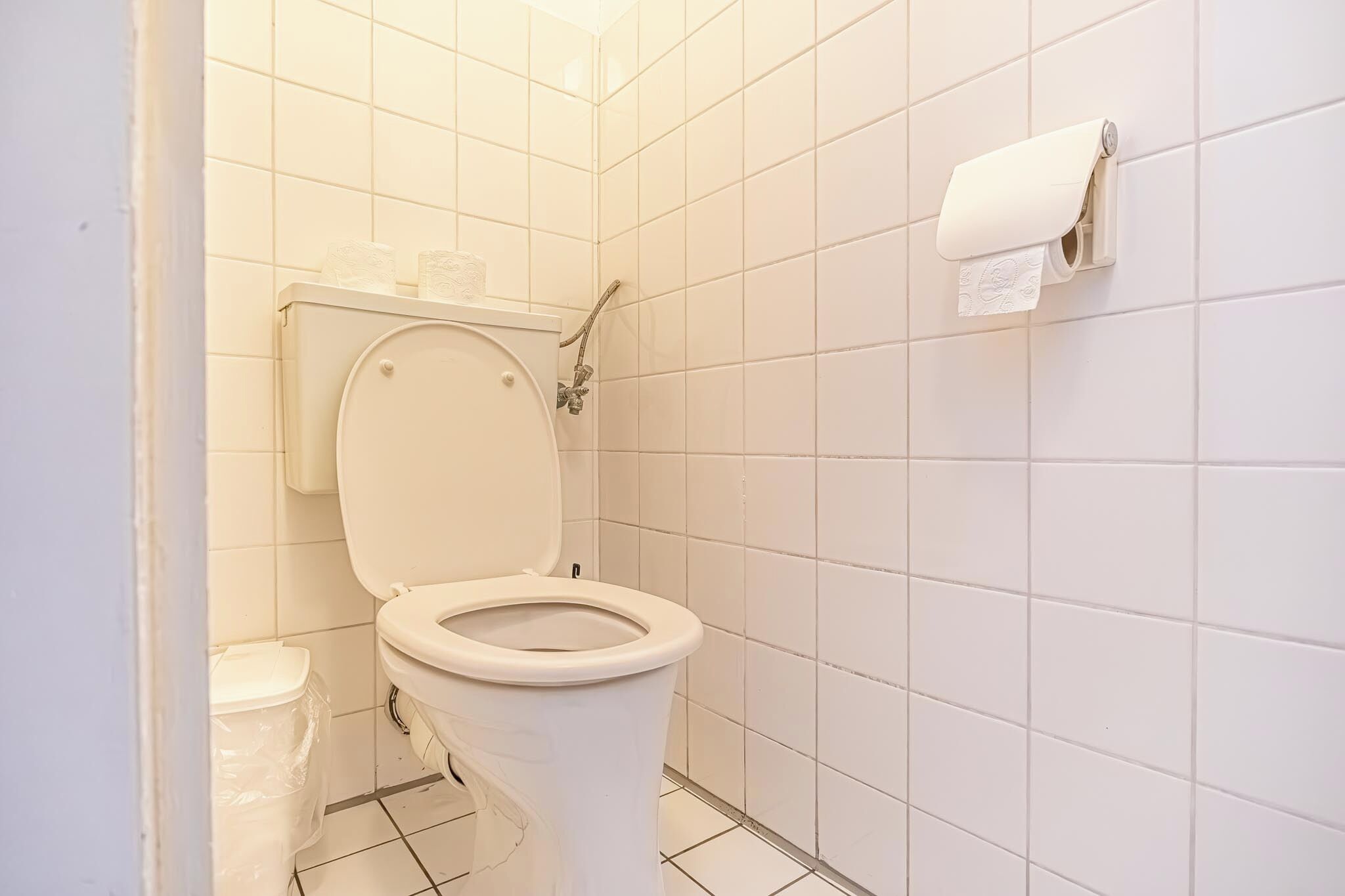 A bathroom with a toilet, a paper towel dispenser, and a plastic trash bin.