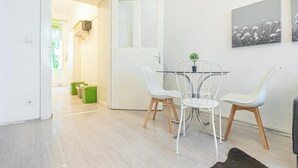 Zona pranzo moderna con tavolo in vetro e sedie bianche, una porta che dà su un'altra stanza e due opere d'arte appese al muro.