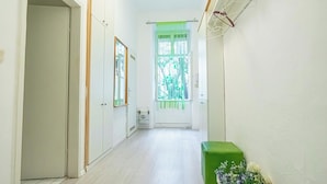 Un corridoio stretto con pareti bianche, una panca verde e una finestra con tenda verde.