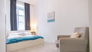 Una camera da letto con un letto, una sedia, una lampada e un quadro appeso al muro.