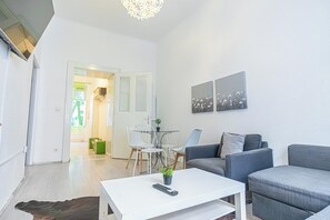 A modern living room with a grey sofa, a white coffee table, and a dining area with a small table and chairs. - Budget 1BR Near Belvedere Palace (Vienna)
