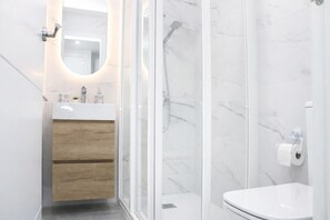 Ein modernes Badezimmer mit Duschkabine aus Glas, einem Holzausleger und einer Wand mit Marmorplatten.