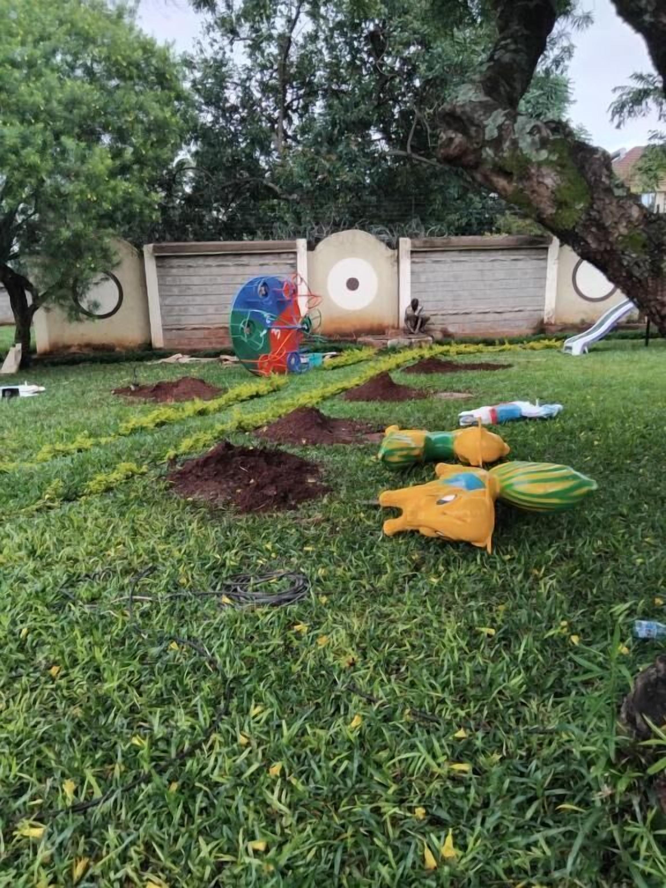 A grassy outdoor area with a playground structure, a wall with circular designs, and a tree.