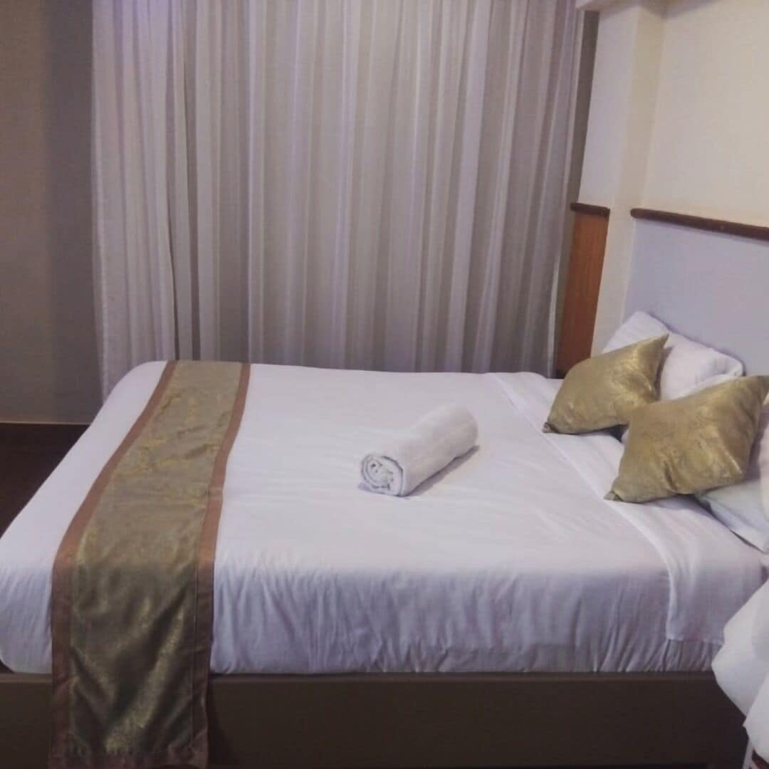 Una habitación de hotel con una cama bien hecha, una toalla enrollada y dos almohadones decorativos.