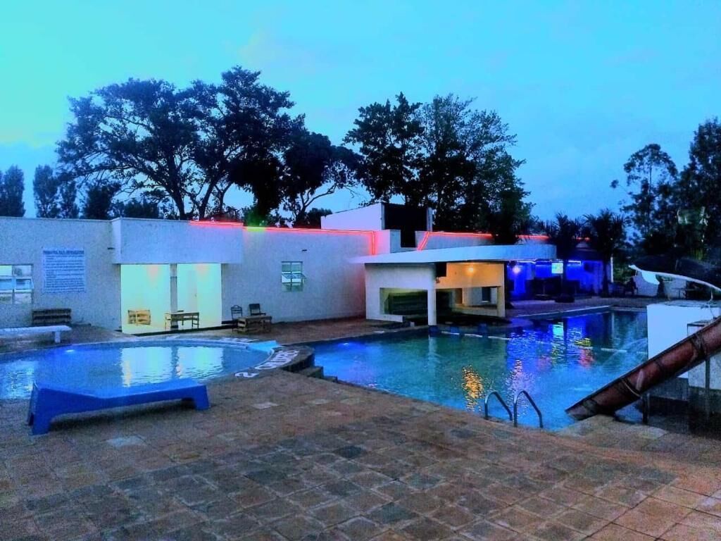 A swimming pool area with a lounge chair, a small building with a door, and a slide.