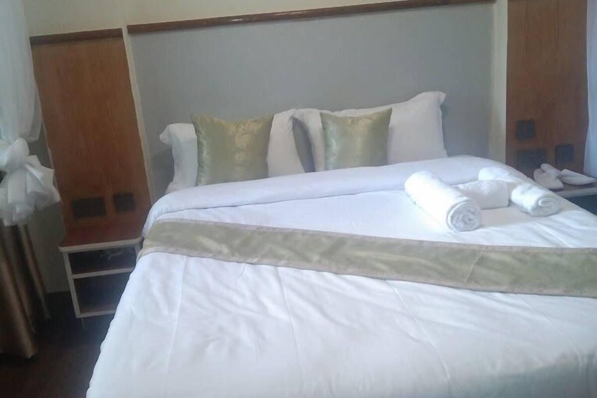 A hotel room with a large bed, a wooden headboard, and a bedside table with a lamp.