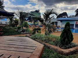 Zona junto a la piscina con sillas de descanso, una terraza de madera y vistas a edificios y árboles.