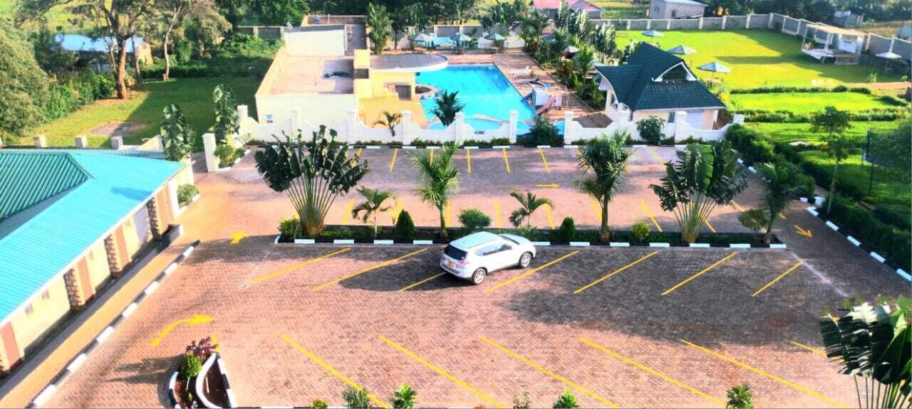 A hotel with a swimming pool, a parking area, and a building with a green roof.