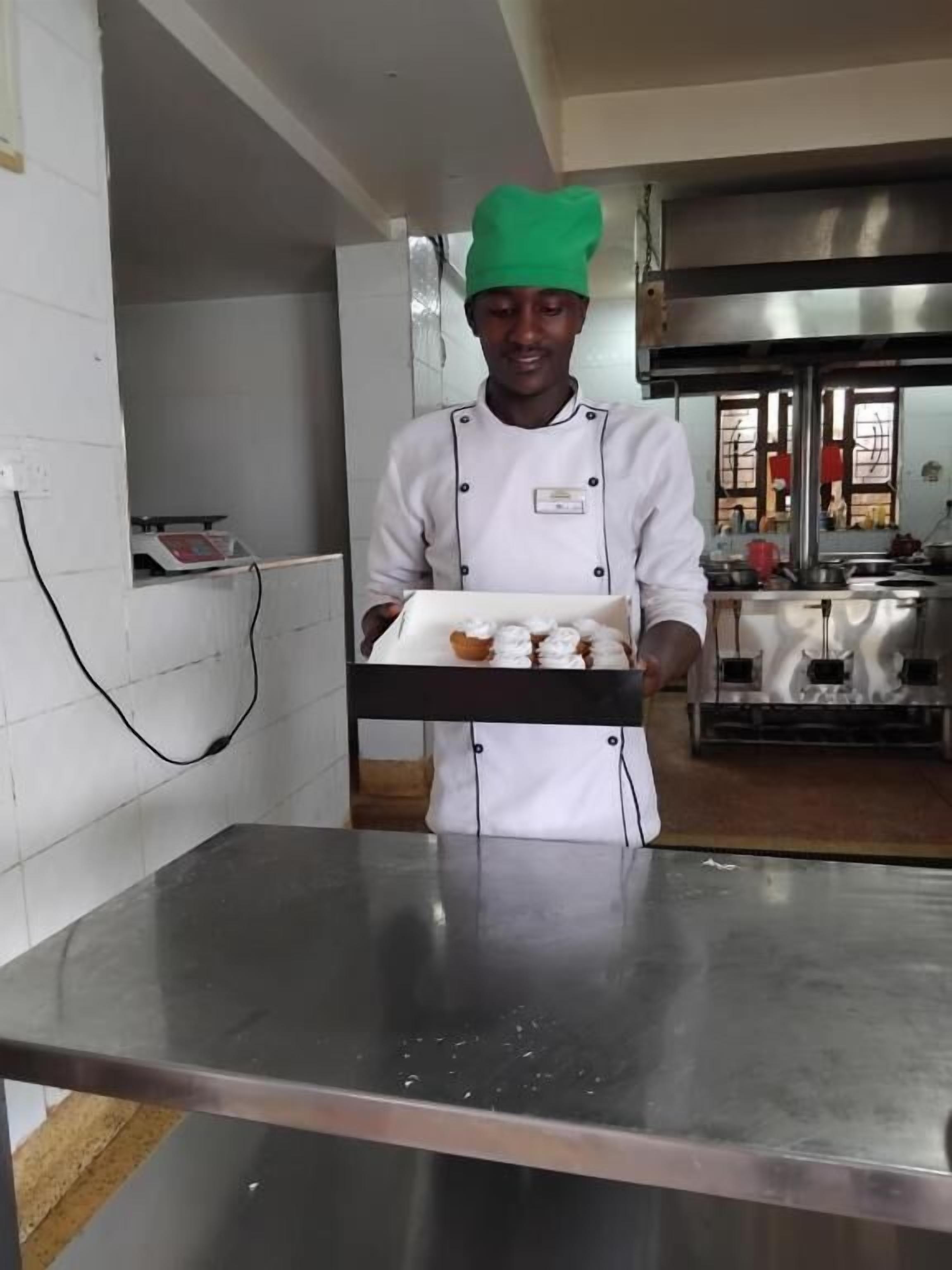 A chef in a white uniform with a green hat holding a tray with pastries.