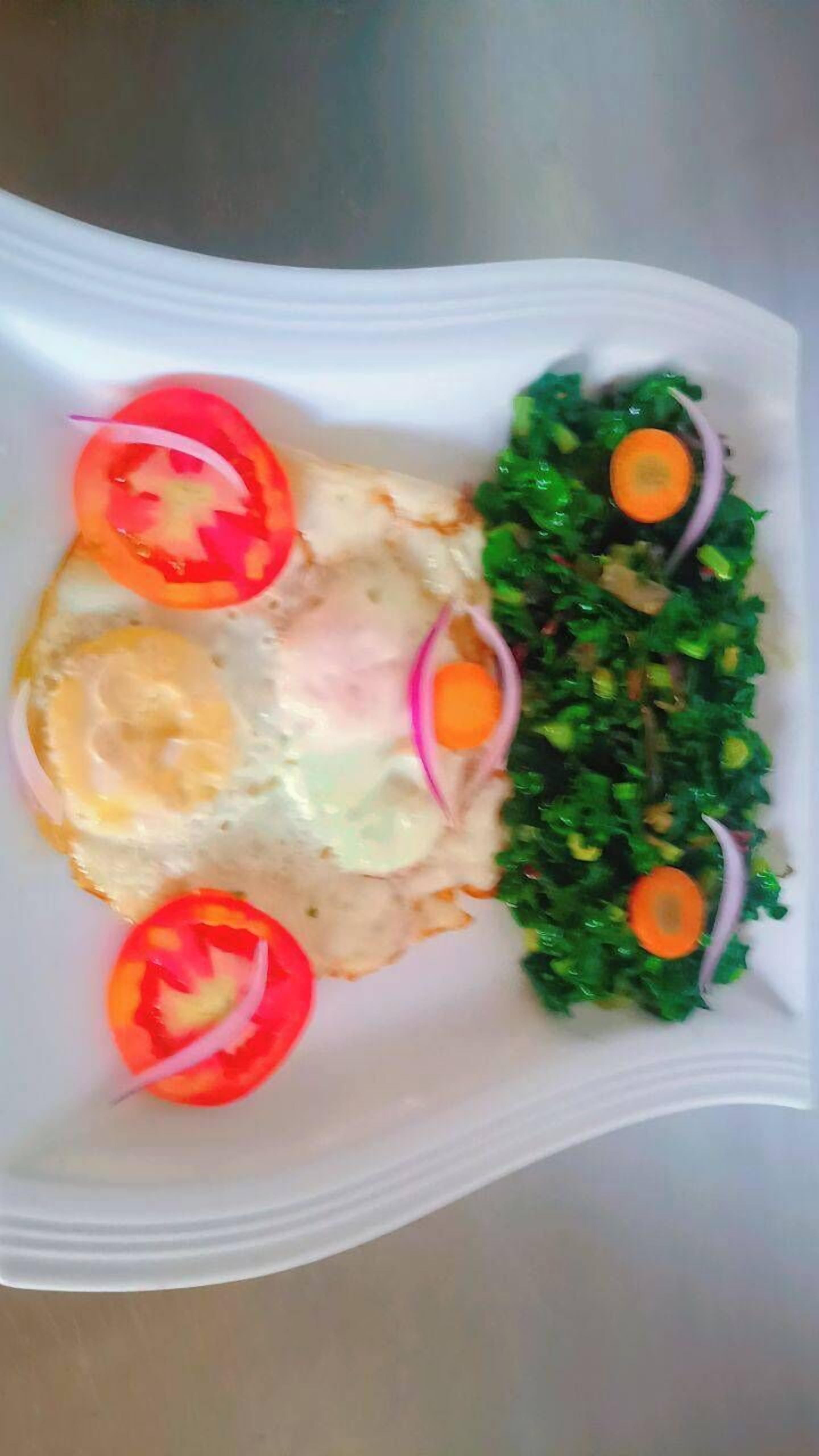 Une assiette blanche contenant un œuf au plat, des tranches de tomate et une salade composée de légumes verts et de carottes.