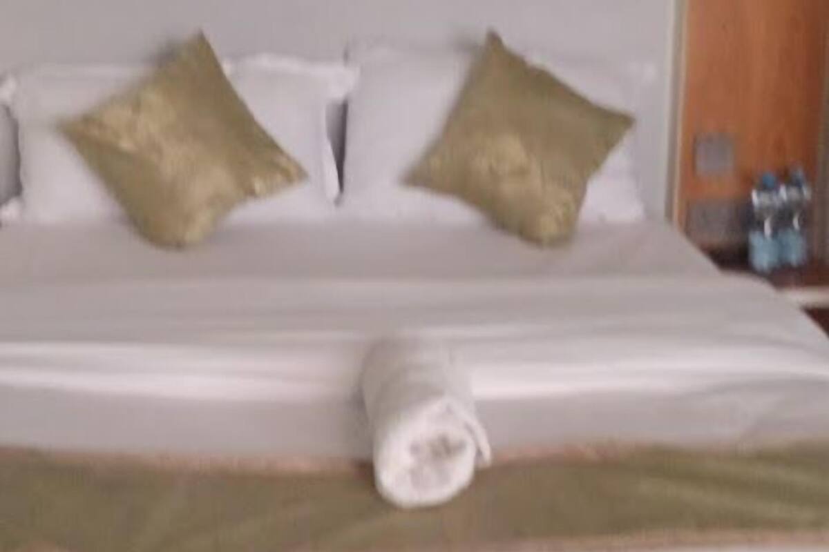 A neatly made bed with white linens and two gold pillows.