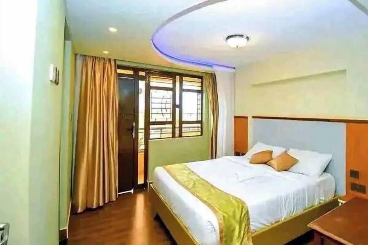 A hotel room with a bed, curtains, a window, and a ceiling light.