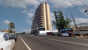 Un edificio alto con varios balcones, cielo despejado y una calle con coches estacionados.