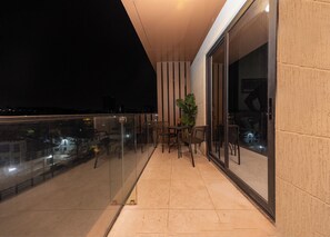Ein Balkon mit Glasgeländer, einem Blumentopf und mehreren Stühlen.