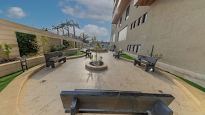 Un patio con bancos, una jardinera circular y un edificio con grandes ventanales.