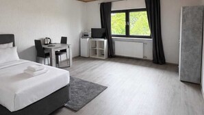 A modern hotel room with a wooden ceiling, a large bed, a desk with a chair, a radiator, and a window with curtains. - Frankfurt West Family Stay (Kelsterbach)