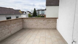A rooftop patio with tiled flooring, a brick wall, and a white building with a tiled roof. - Frankfurt West Family Stay (Kelsterbach)