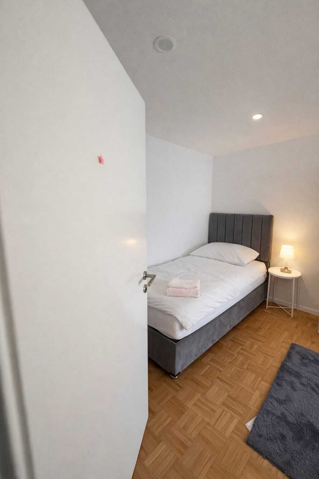 Un dormitorio con cama, mesita de noche con lámpara y suelo de madera.