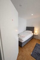 Un dormitorio con cama, mesita de noche con lámpara y suelo de madera.
