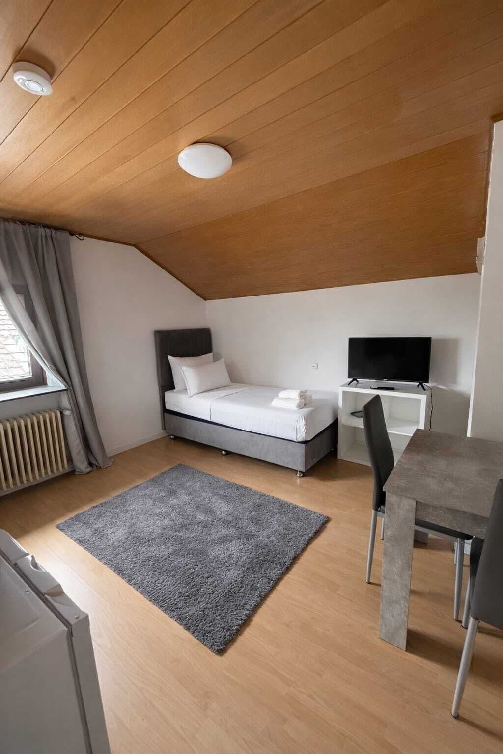Ein kleines, modernes Schlafzimmer mit Bett, Nachttisch und Schreibtisch mit Stuhl.