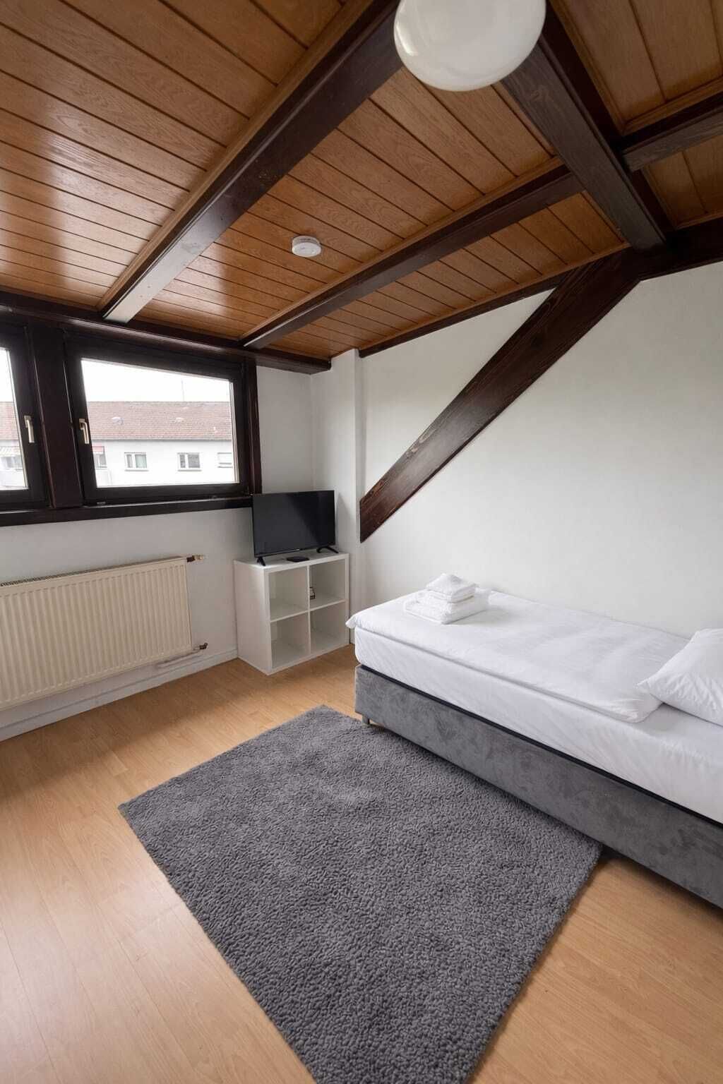 Een slaapkamer met een schuine kap, een bed, een televisie, een radiator en een raam.