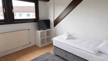 Een slaapkamer met een schuine kap, een bed, een televisie, een radiator en een raam.