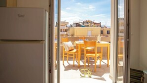 Ein Balkon mit Tisch und Stühlen, einem Kühlschrank und Blick auf Gebäude im Hintergrund.