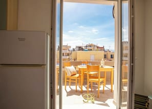 Ein Balkon mit Tisch und Stühlen, einem Kühlschrank und Blick auf Gebäude im Hintergrund.
