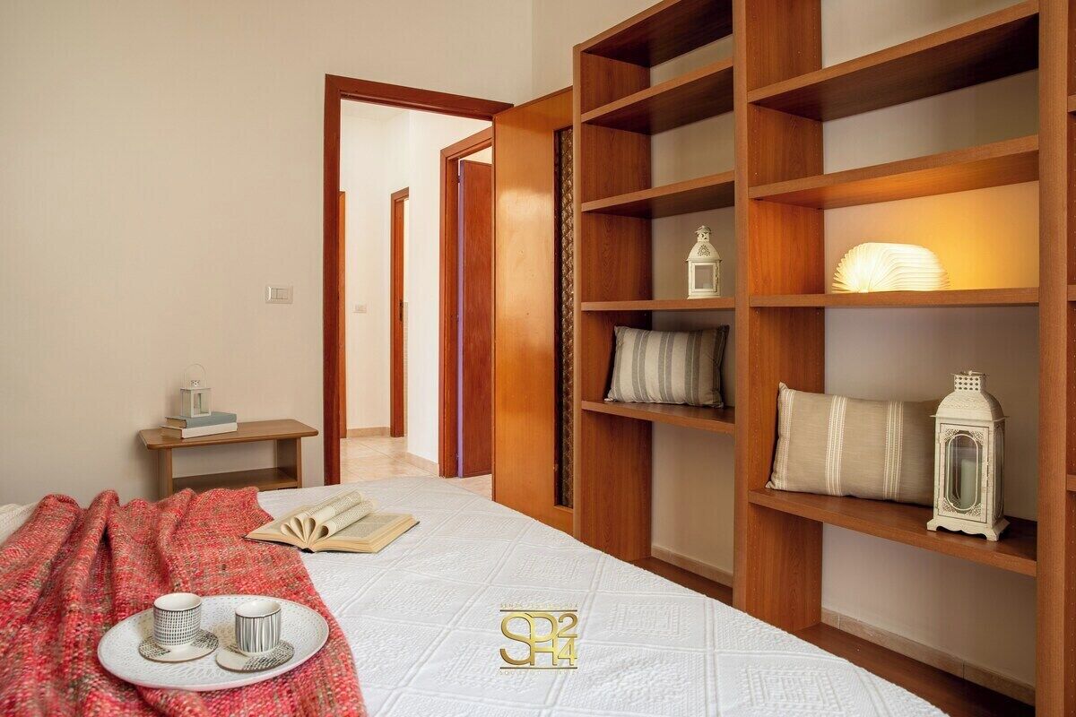 Een keurig opgemaakt slaapkamer met een bed, een nachtkastje met een lamp en een plank met decoratieve objecten.