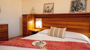 Ein ordentlich bezogenes Bett mit einer roten und weißen Bettdecke, einem Holz-Kopfbrett und einem kleinen Nachttisch mit einer Lampe.