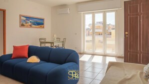 Ein Wohnzimmer mit blauem Sofa, rotem Kissen, einem Gemälde und einem Essbereich mit Stühlen und Tisch.
