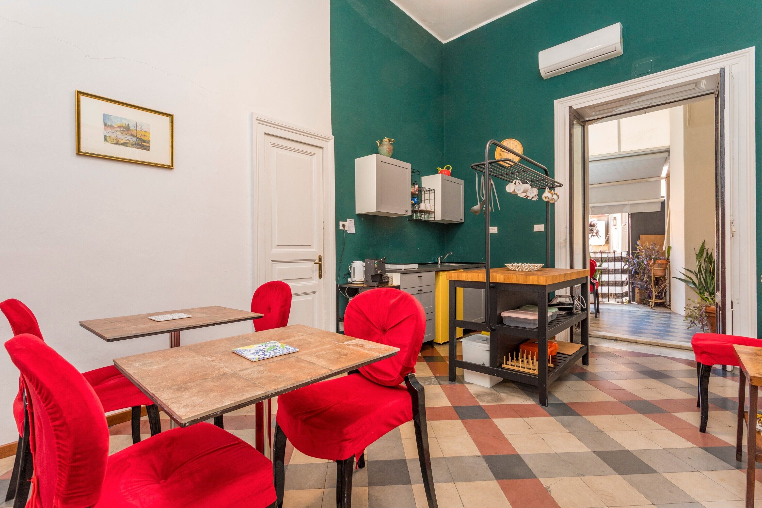 Un coin repas avec des chaises rouges, une table en bois et un sol à carreaux. On y trouve également un espace cuisine avec des placards et une étagère.
