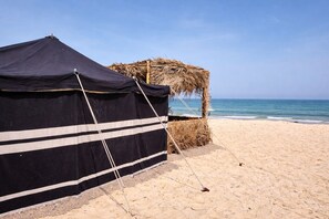 Una playa con una carpa negra y una estructura de paja.