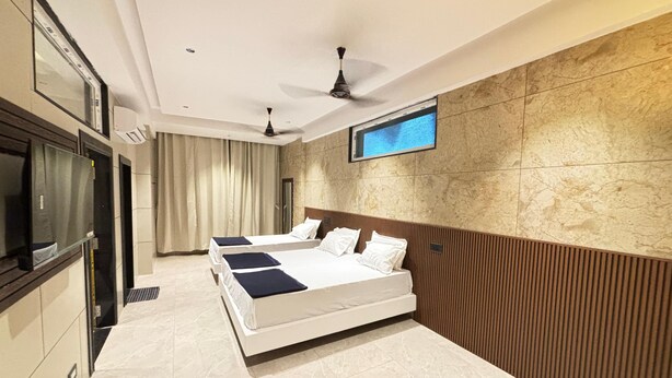 A modern hotel room with a large bed, a TV mounted on the wall, and a ceiling fan. - Sreeniketanam Lodge (Mantralayam)