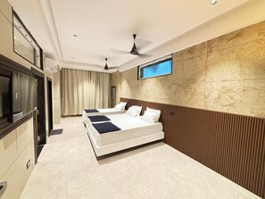 A modern hotel room with a large bed, a TV mounted on the wall, and a ceiling fan. - Sreeniketanam Lodge (Mantralayam)