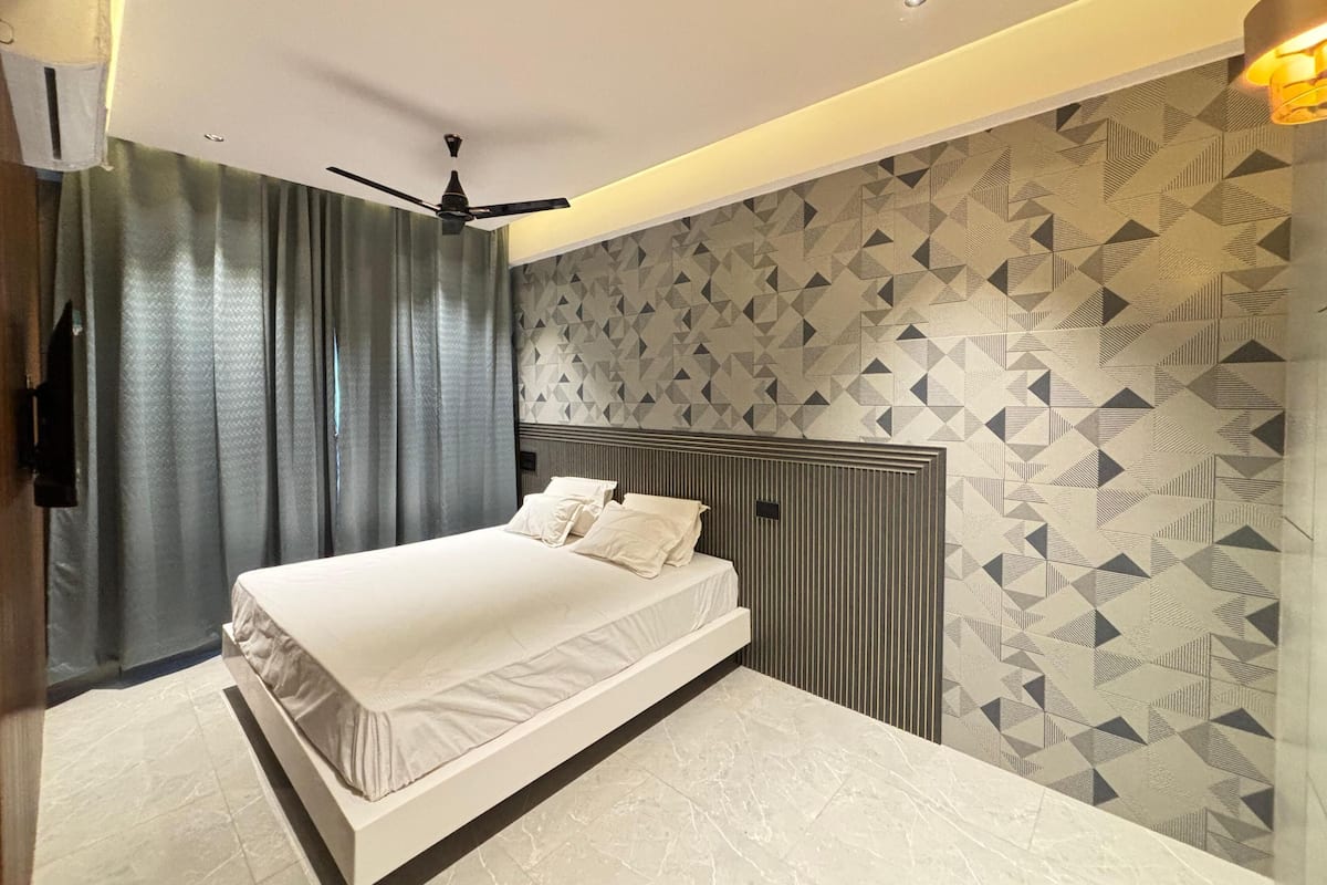 Une chambre à coucher moderne avec un grand lit, un ventilateur de plafond et un papier peint à motifs.