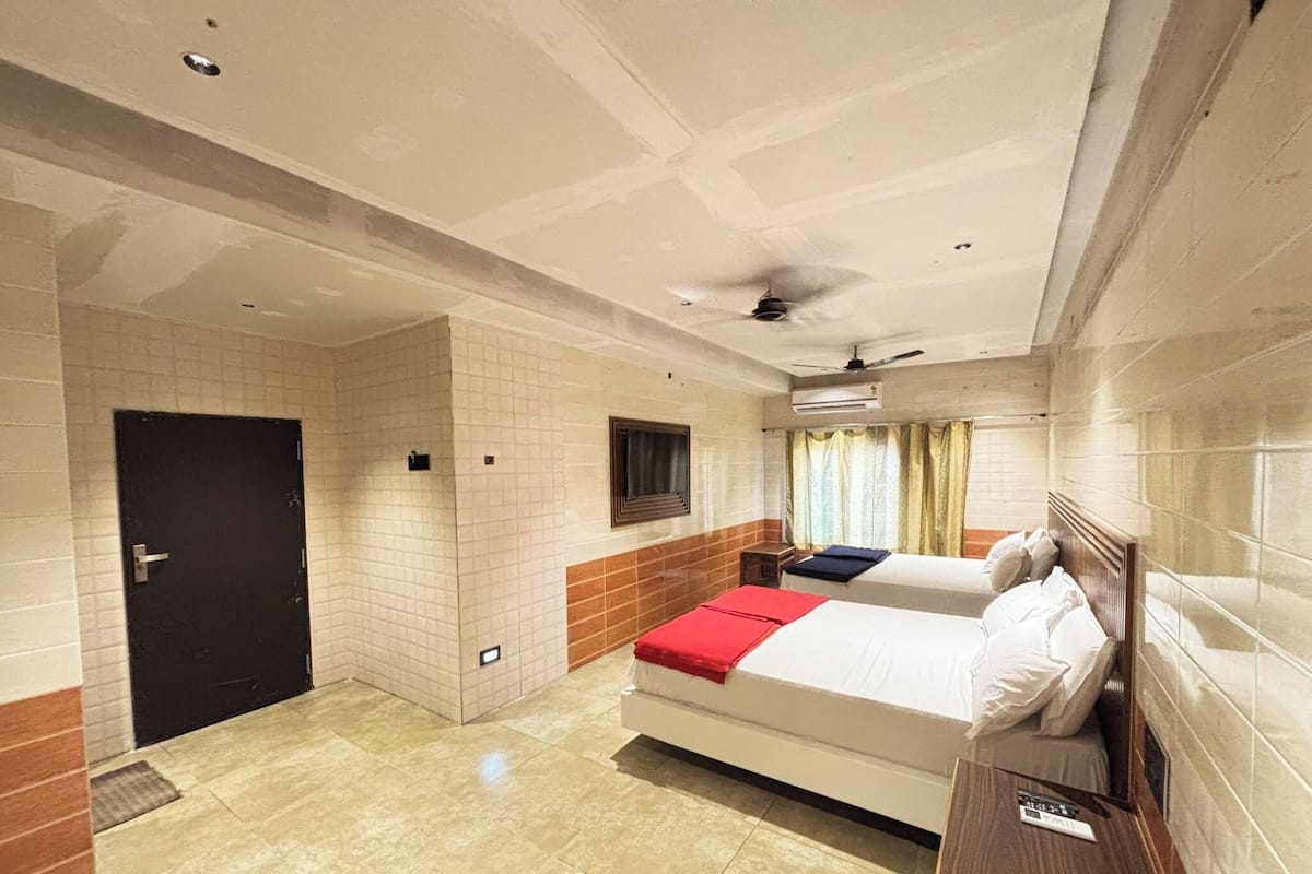 Une chambre d’hôtel avec deux lits, un ventilateur de plafond, un appareil de climatisation et une fenêtre avec des rideaux.