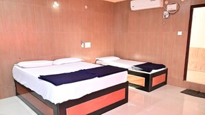 A hotel room with two beds, a mirror, a wall-mounted air conditioner, and a door leading to a balcony. - Sreeniketanam Lodge (Mantralayam)