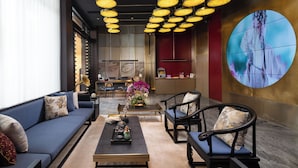 A modern hotel lobby with a sofa, chairs, a coffee table, and a large screen displaying a person. - The Yun Collection  Yongqingfang  (Guangzhou)