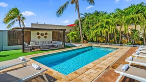 Une piscine avec des chaises longues et un espace de détente couvert, agrémenté de coussins.