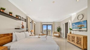 Une chambre spacieuse avec un grand lit, une tête de lit en bois, une armoire en bois et un téléviseur fixé au mur.